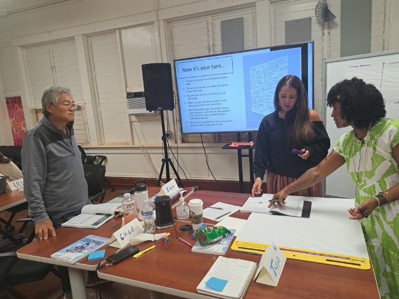 One man and two women standing around table working on project