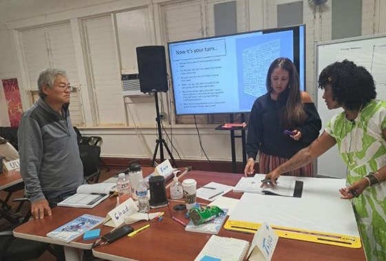 One man and two women standing around table working on project